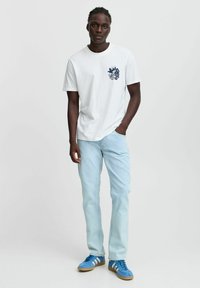 Camiseta de algodón blanca con un gráfico en color marino en el pecho, combinada con unos vaqueros de denim de color azul claro y zapatillas azules con franjas blancas.