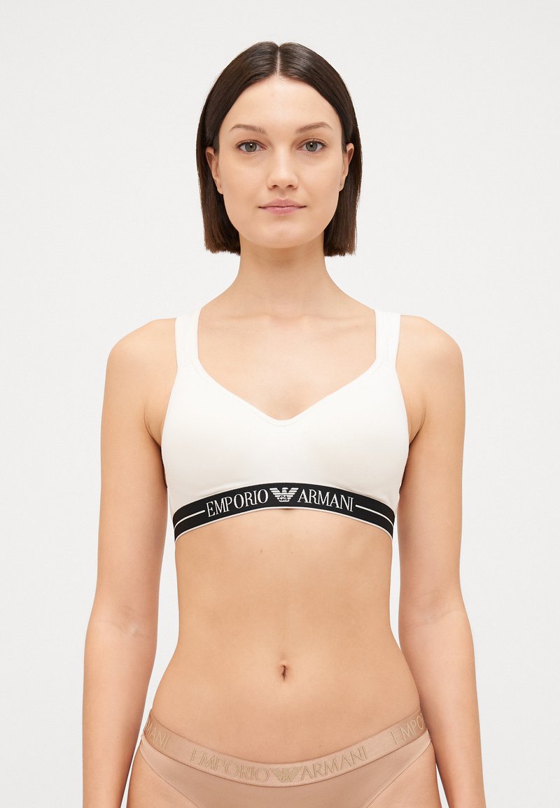 Light beige bralette with a soft, smooth fabric. It features a black elastic band with "Emporio Armani" logo and wide adjustable straps.