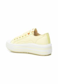 Zapatillas de lona amarillas con suela de goma blanca, diseño curvado, ojales naranjas para los cordones y sutiles rayas diagonales en la suela.