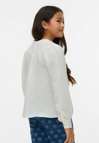 Blusa bianca a maniche lunghe con trama, collo rotondo e polsini con bottoni, abbinata a jeans blu con motivo a cuore.