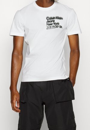 Biała bawełniana koszulka z krótkim rękawem z czarnym nadrukiem: "Calvin Klein Jeans New York 205 W39 St." Okrojny dekolt.