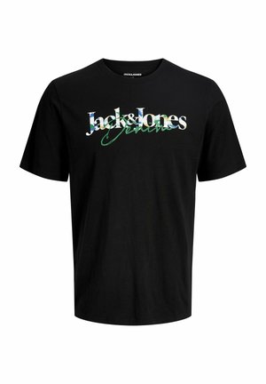 Ξανθό αγόρι που χαμογελά, φοράει μαύρο T-shirt Jack & Jones, άνετα μπλε τζιν και μπεζ αθλητικά παπούτσια, στέκεται μπροστά σε απλό φωτεινό φόντο.