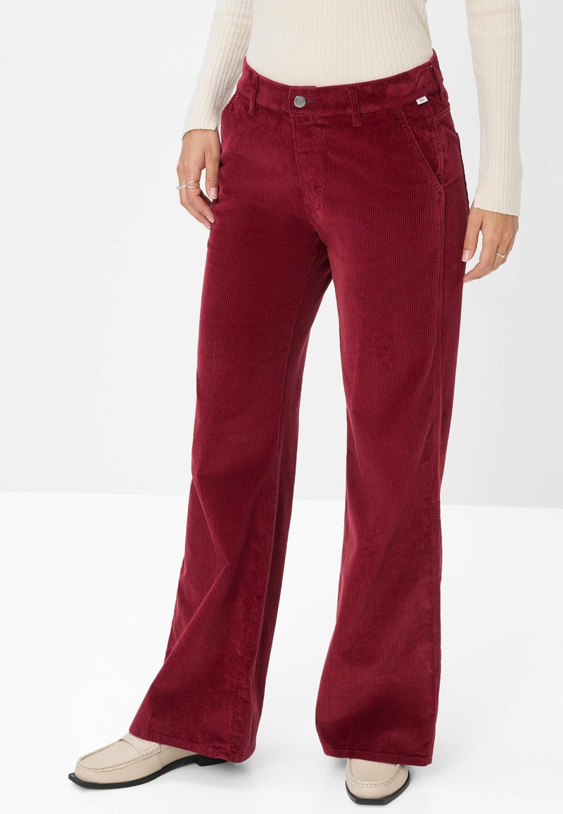Rode corduroy wijde broek met een textuurafwerking, voorzien van voorzakken en een knoopsluiting. Gecombineerd met een strakke crèmekleurige top.