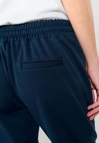 Pantalones de chándal azul marino con un ajuste relajado, que cuentan con una cinturilla elástica y un pequeño bolsillo trasero. Fabricados con una tela suave de textura lisa.