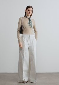 Μπεζ μακρυμάνικο τοπ με φουλάρι σε πράσινο μοτίβο, συνδυασμένο με λευκό παντελόνι ψηλόμεσο, φαρδύ με μεγάλες τσέπες και λεία υφή.