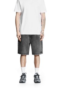 Czarne szorty dżinsowe o prostym kroju, noszone z gładką białą koszulką. Obuwie to szare sneakersy i białe skarpetki do kostek.