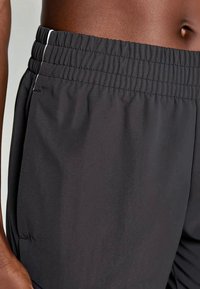 Pelēkā sporta šortos ar elastīgu jostasvietu un baltu akcentu šuvēm. Audums izskatās gluds un viegls.