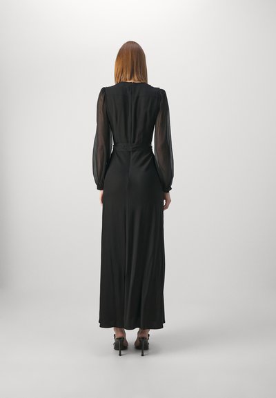 Robe maxi noire avec de longues manches transparentes, corsage ajusté et taille cintrée ; tissu lisse avec une jupe fluide, associée à des talons hauts.