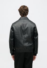 Giubbotto in pelle nera con design a colletto, vita a costine e texture liscia. I dettagli cuciti valorizzano la silhouette moderna.