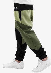 Pantaloni jogger conici, verzi și negri, cu un finisaj texturat, dotati cu buzunare laterale și o talie elastică. Asortați cu teneși albi.