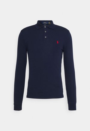 Polo bleu marine à manches longues avec trois boutons et un petit logo rouge brodé sur la poitrine gauche.
