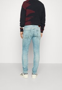 Světlé modré džíny slim fit, pět kapes a kontrastní švy. Přiřazeny s černým a vínovým vzorovaným svetr a bílými teniskami.