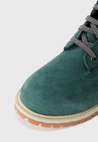 Stivale alla caviglia verde in camoscio con tomaia testurizzata, dotato di lacci a righe bianche e nere e una suola in gomma a contrasto con motivo scanalato.