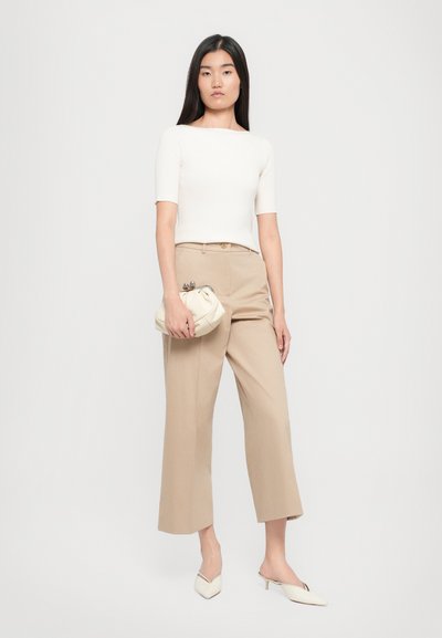 Top bianco a coste a maniche corte, pantaloni beige a gamba larga e borsa color crema. Il modello indossa mule bianche a punta, design minimalista e chic.