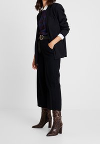 Black blazer over a plaid shirt, high-waisted black wide-leg pants, and brown snake-print heeled boots with a pointed toe.