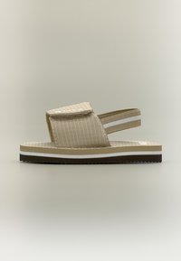 Μπεζ ρυθμιζόμενο σανδάλι ανοιχτής μύτης με παχύ πέλμα, υφασμάτινο λουράκι πάνω από το πόδι με βέλκρο και ελαστικό πίσω λουράκι με λευκή ρίγα.