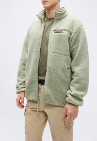 Ζεστό μπουφάν φλις σε ανοιχτό πράσινο χρώμα, με φερμουάρ μπροστά, ψηλό γιακά και τσέπη στο στήθος. Μαλακή υφή με ριμπ μανσέτες και τελείωμα.