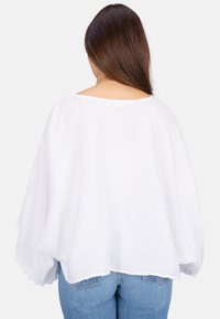 Weiße, leichte, oversized Bluse aus strukturiertem Stoff mit rundem Ausschnitt. Der Saum ist mit zarter Spitze verziert. Tragen Sie sie mit blauen Jeans.