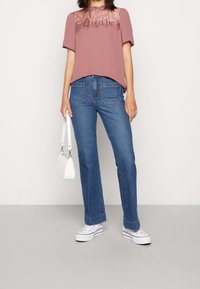 Světle růžové tričko s krajkovým zdobením kolem výstřihu, kombinované s modrými džíny a bílými teniskami. Doplňek: malá bílá kabelka.