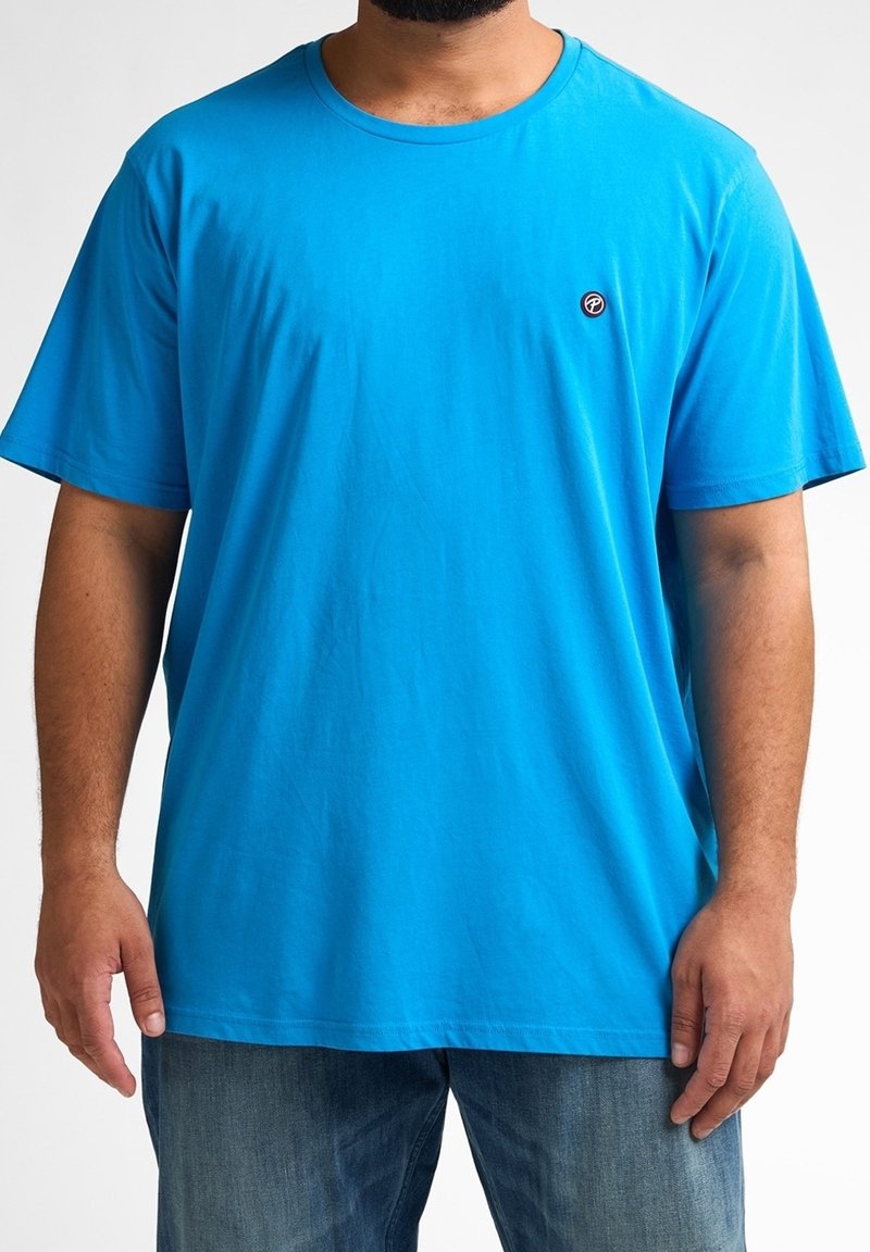 Camiseta de algodón de manga corta y cuello redondo en un brillante color azul, con un parche de logo en el lado izquierdo del pecho. Presenta un ajuste relajado y una textura suave.