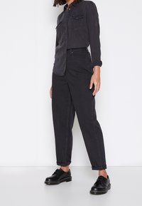 Svart denimskjorta med knappstängning och två bröstfickor, i kombination med löst sittande svarta jeans och svarta snörskor.