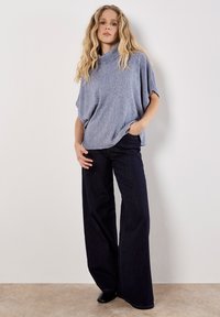 Hellblaues, strukturiertes Strickoberteil mit einem Schalkragen, kombiniert mit dunkelblauen, weit geschnittenen Jeans. Das Outfit hat eine lässige Passform und seitliche Taschen.