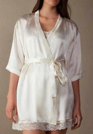 Satinge Kremschimmerkimono mit kurzen Ärmeln, tailliertem Gürtel und Spitzenbesatz am Saum. Weiche Textur und glatte Oberfläche.