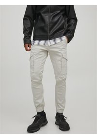 Vaaleanbeige cargo-housut, joissa on elastiset hihnat, useilla sivutaskuilla, yhdistetty mustaan nahkatakkiin ja mustiin lenkkareihin.