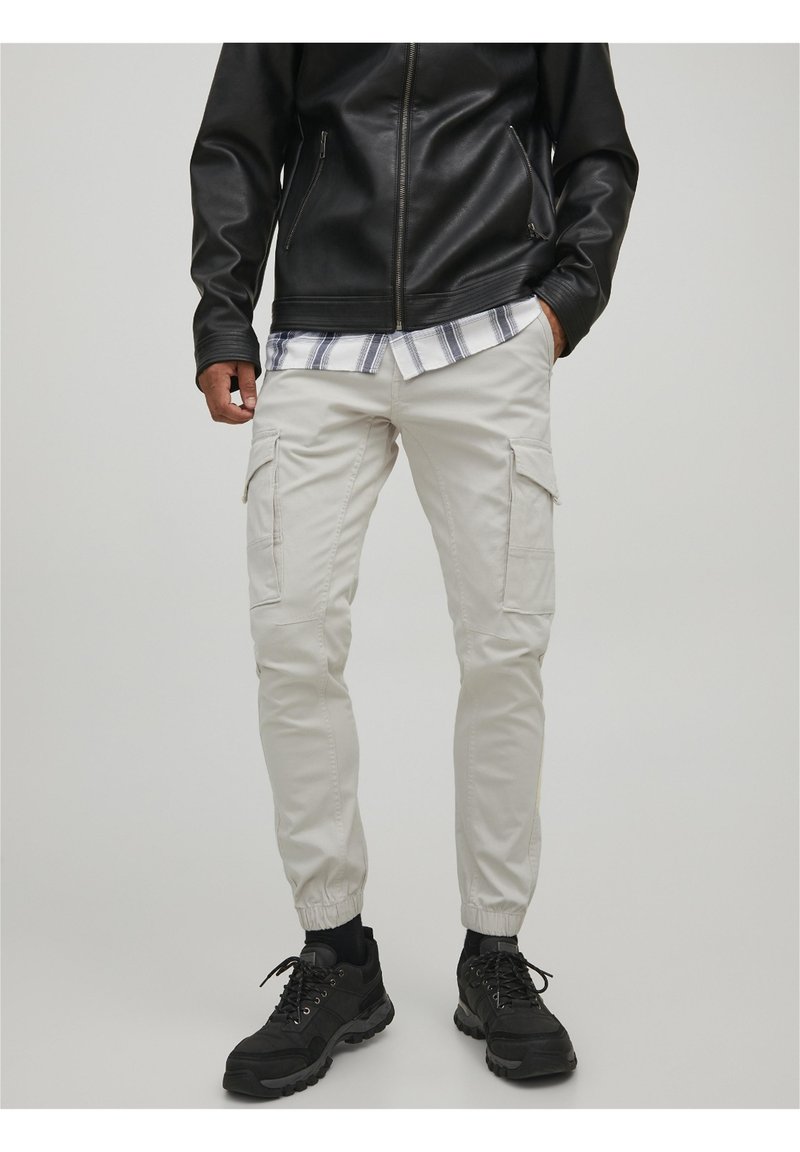 Vaaleanbeige cargo-housut, joissa on elastiset hihnat, useilla sivutaskuilla, yhdistetty mustaan nahkatakkiin ja mustiin lenkkareihin.