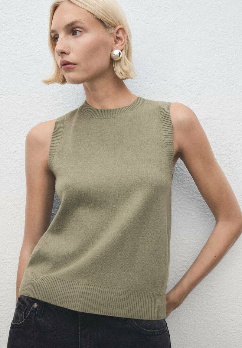 Top fără mâneci de culoare verde măsliniu, din tricot, cu decolteu rotund și margini cu dublu tors, asortat cu blugi închisi. Design minimalist cu textură netedă.
