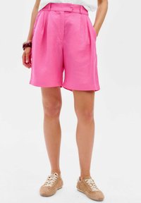 Roze geplooide shorts van lichtgewicht stof met een gladde textuur. Heeft een hoge taille en zijzakken, gecombineerd met beige sneakers.