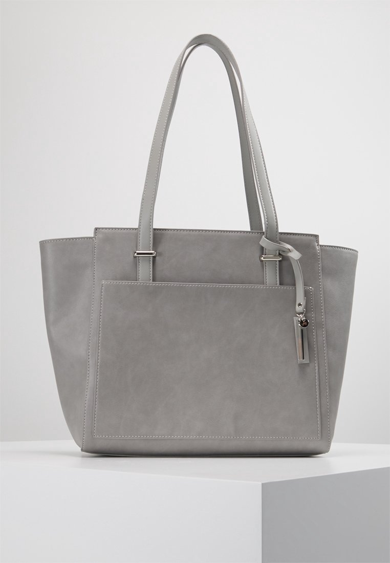 Sac fourre-tout en cuir gris avec double poignée et poche avant, exposé sur un piédestal blanc sur fond neutre.