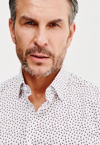 Biała koszula z guzikami z małym, powtarzającym się wzorem kwiatowym w ciemnoczerwonym kolorze. Miękki materiał z klasycznym kołnierzykiem i zapięciem na guziki.