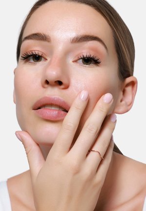 Modella con pelle liscia, trucco naturale e unghie rosa chiaro, che indossa un sottile anello in oro rosa ondulato. Lo sfondo è bianco semplice.