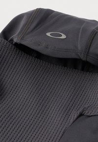 Fekete, texturált anyag sima kapucnival, varrott ovális logóval, amely az anyag részleteire és a varrás kialakítására fókuszál.