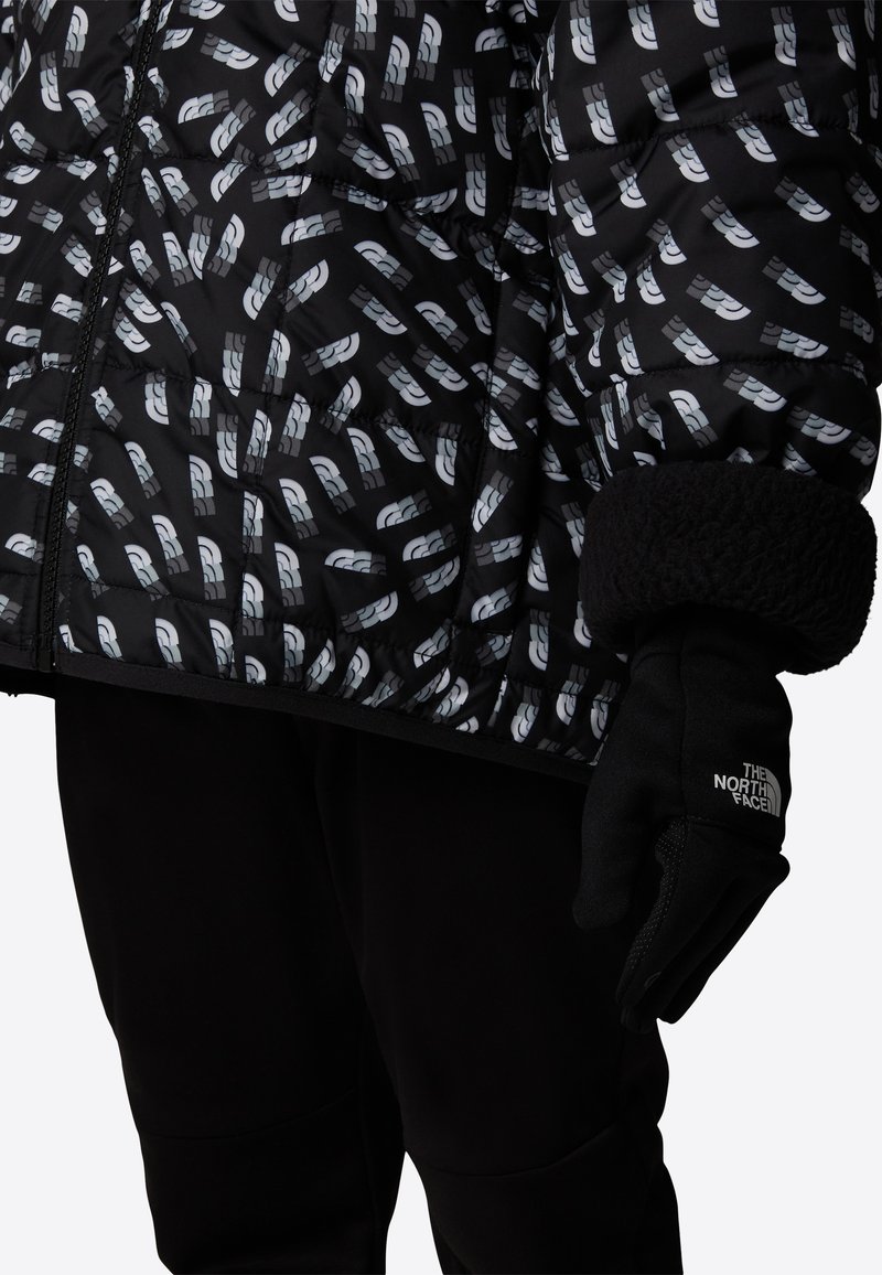 Svart vattert jakke med hvitt geometrisk mønster, quiltet design og myke svarte mansjetter. Komplett med en svart hanske med en logo.