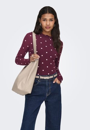 Bordeaux rød langærmet top med ribstruktur og hvide prikker, kombineret med vide blå denimbukser og en beige skuldertaske.