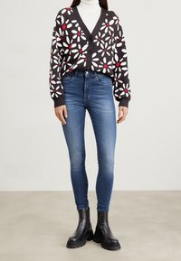 Knitted black cardigan with white and red floral pattern, paired with fitted blue jeans and black ankle boots with chunky soles.