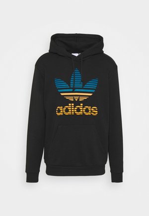 Schwarzer Adidas Hoodie mit blau-gelbem gestreiftem Trefoil-Logo und Fronttasche, dargestellt auf einem einfarbigen hellen Hintergrund.