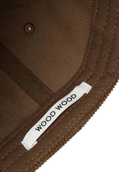 Barna textil sapka vízálló anyaggal, kontrasztos fehér címkével, amelyen feketével van hímezve a "WOOD WOOD" felirat, valamint látható varrási részletekkel.