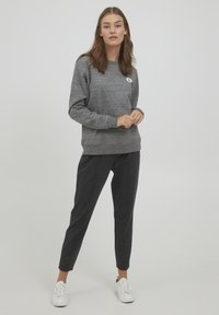 Grå hettegenser med teksturert stoff og rund lapp, kombinert med mørke smale bukser og hvite sneakers. Enkelt, uformelt antrekk.