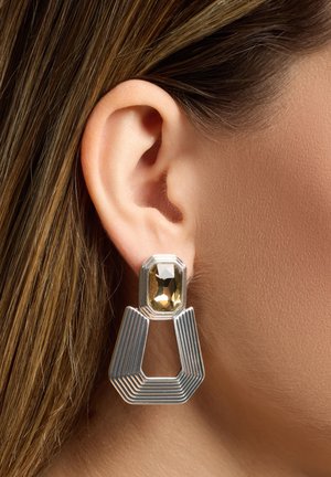 Pendientes geométricos de plata con un diseño texturizado, que cuentan con una gran gema rectangular amarilla en la parte superior.