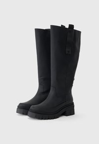 Schwarze kniehohe Stiefel aus glattem, mattem Material. Dicke, geriffelte Sohle und ein Stoffzugband auf der Oberseite für einfaches Anziehen.