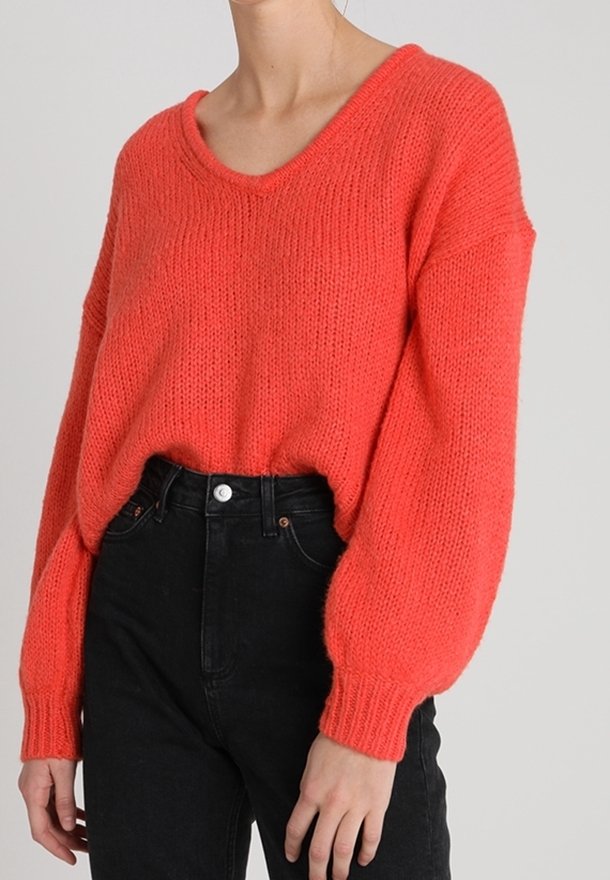 Maglione in maglia corallo con scollo a V, vestibilità ampia e maniche lunghe e voluminose, abbinato a jeans neri a vita alta. Tessuto morbido e dettaglio a coste.