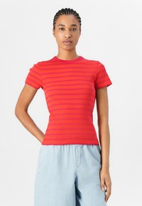 Haut rouge à manches courtes côtelé avec des rayures horizontales roses. Design ajusté et col rond, associé à un pantalon large bleu clair.