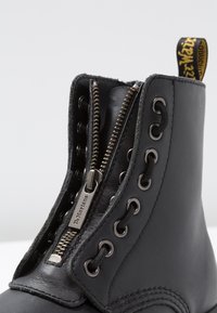 Mustmust mustat, millel on külgriie, ümmargused metallist silmad ja tekstuuriga viimistlus. Includes a branded pull tab at the heel.