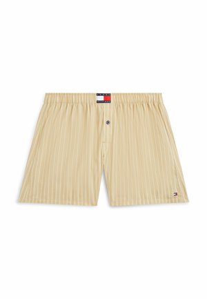 Beżowe bawełniane bokserki w paski z elastycznym pasem, pojedynczym niebieskim guzikiem na rozporku oraz małymi naszywkami z logo Tommy Hilfiger na pasie i dolnej krawędzi.