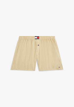 Beżowe bawełniane bokserki w paski z elastycznym pasem, pojedynczym niebieskim guzikiem na rozporku oraz małymi naszywkami z logo Tommy Hilfiger na pasie i dolnej krawędzi.