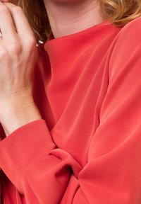 Czerwony, lekki materiał o gładkiej teksturze i swobodnym kroju. Posiada luźne rękawy i marszczone detale, które dodają objętości.