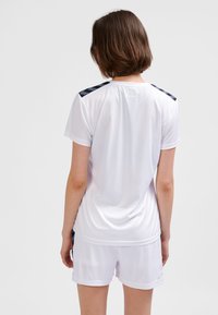 Biały sportowy T-shirt z krótkimi rękawami, ozdobiony czarnymi wzorzystymi akcentami na ramionach; w połączeniu z białymi szortami o gładkiej fakturze.